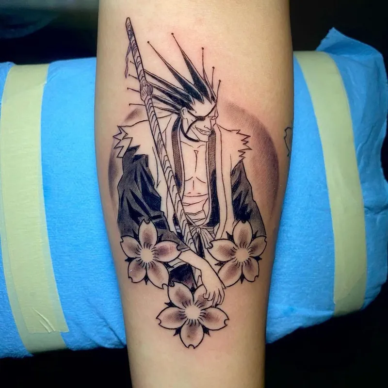 Black and grey anime character tattoo on a forearm, showing a spiky-haired warrior with an eyepatch holding a sword, surrounded by cherry blossoms.