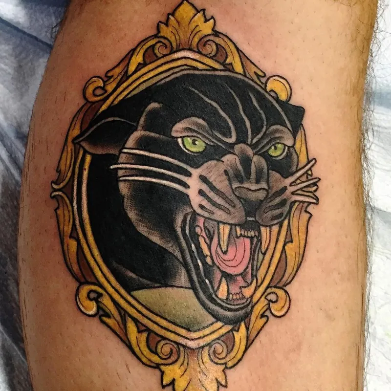 Neo-traditional color tattoo on the calf of a snarling black panther head, framed in an ornate gold mirror shape.