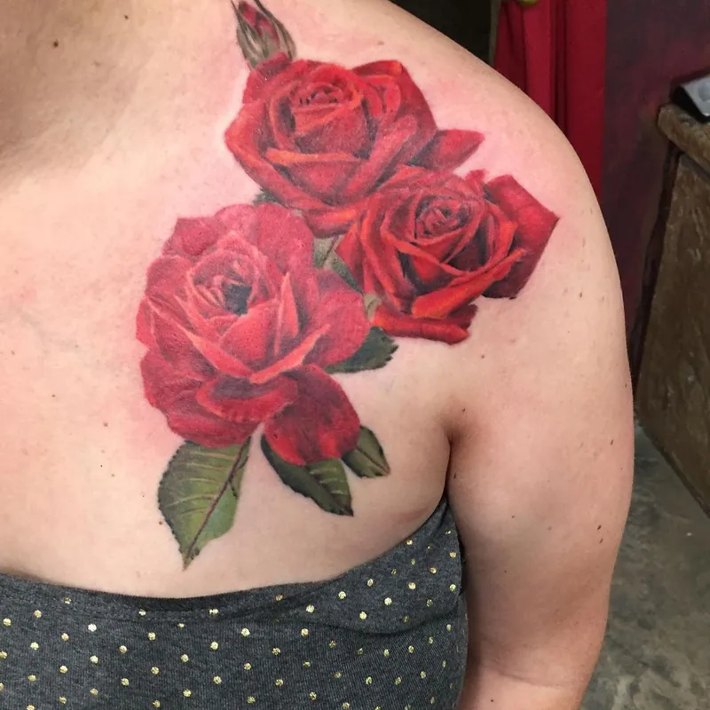 Color realism tattoo on the shoulder blade of three red roses with green leaves.