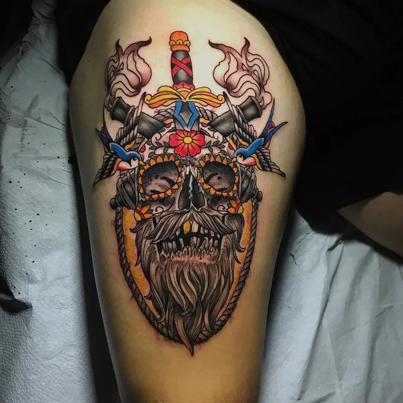 Neo-traditional color tattoo of a bearded skull crowned with a dagger, flanked by crossed pistols and swallows, framed in a rope border on the thigh.
