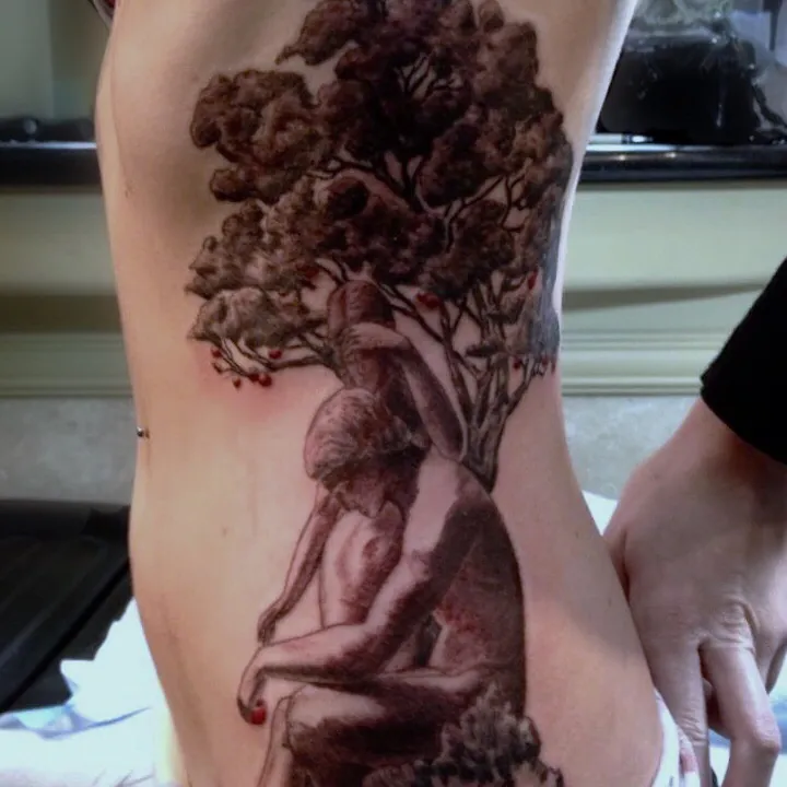 Black and gray realism tattoo on the ribs depicting a man and woman embracing beneath a fruit-laden tree, an Adam and Eve motif.