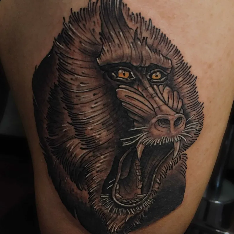 Black and gray tattoo of a roaring mandrill baboon with bared fangs and striking orange eyes, heavy fur texture throughout the mane.