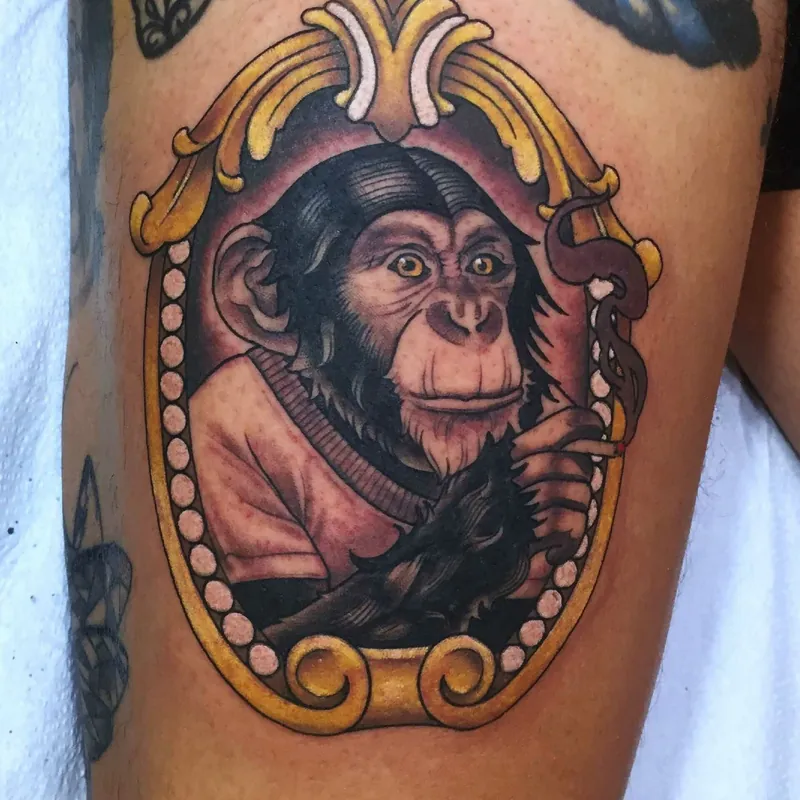 Neo-traditional color tattoo of a chimpanzee in a robe smoking a cigarette, framed in an ornate gold oval on the thigh.