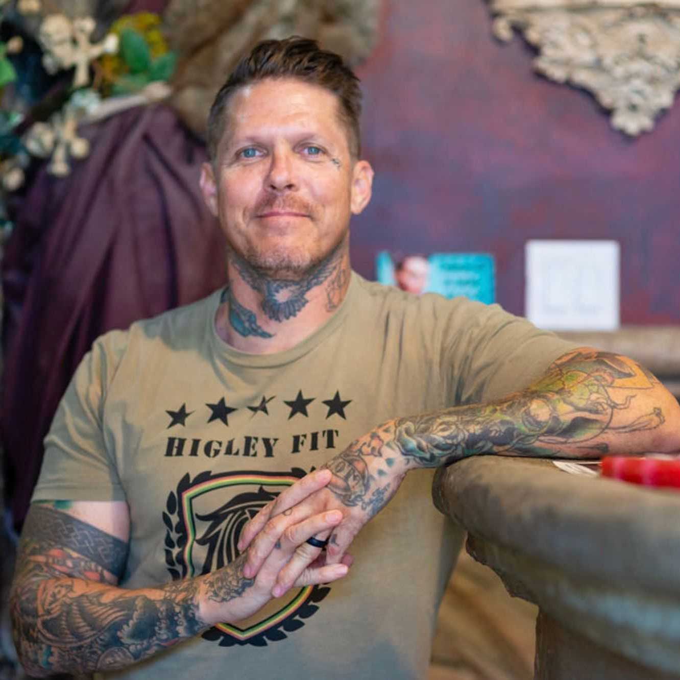 Jason ‘Elvis’ Martin leaning on a counter in his tattoo studio, arms fully sleeved in tattoos