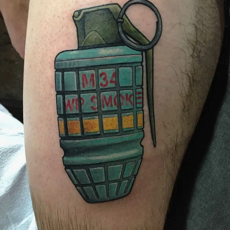 Color traditional tattoo of an M34 smoke grenade with the safety pin and ring pulled loose, on the thigh.