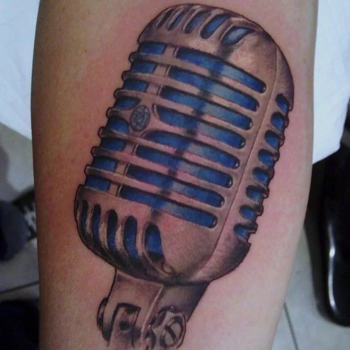 Color realism tattoo of a vintage chrome microphone with a blue-lit ribbed grille and adjustable stand clip, on the forearm.