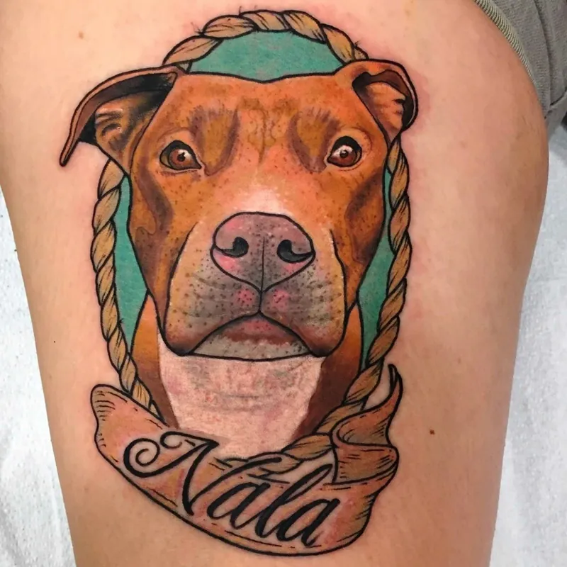 Color neo-traditional tattoo of a pit bull's portrait inside a rope wreath, with a banner reading 'Nala' below, on the thigh.