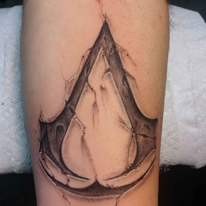 Black and grey tattoo of the Assassin's Creed insignia rendered as though peeling through torn skin, on the forearm.