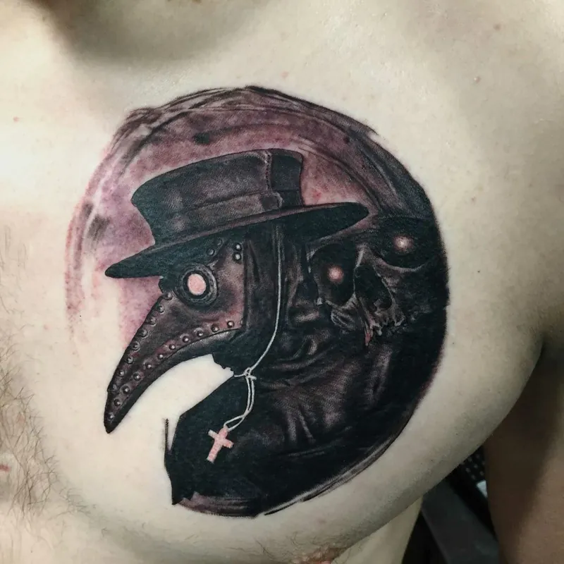 Black and grey tattoo of a plague doctor mask in profile within a moon-shaped frame, with a small skull and cross pendant, on the chest.