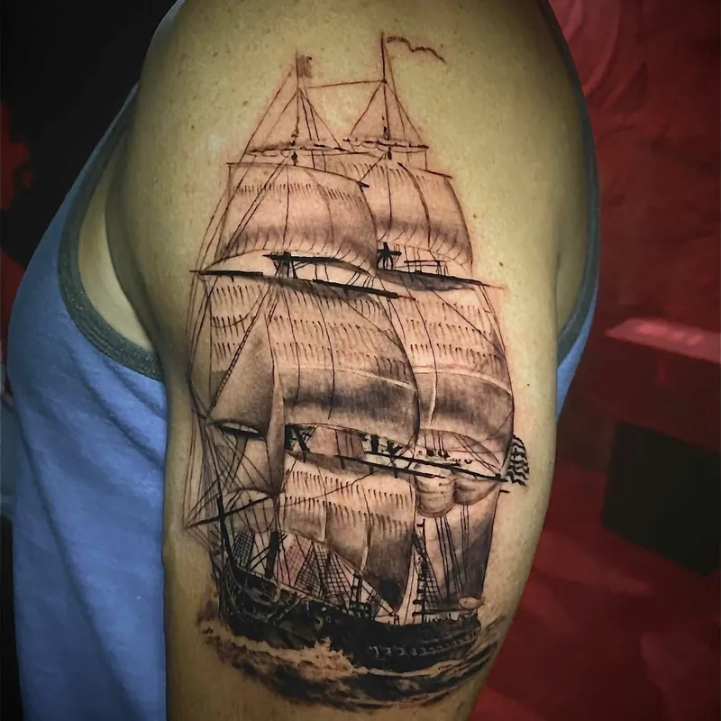 Black and grey tattoo of a full-rigged tall ship under sail on ocean waves, on the shoulder.