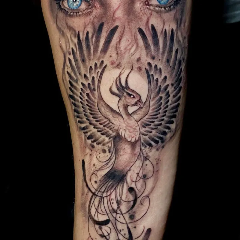 Black and grey tattoo blending a pair of realistic eyes into a phoenix rising with outstretched wings and flowing tail feathers down the forearm.