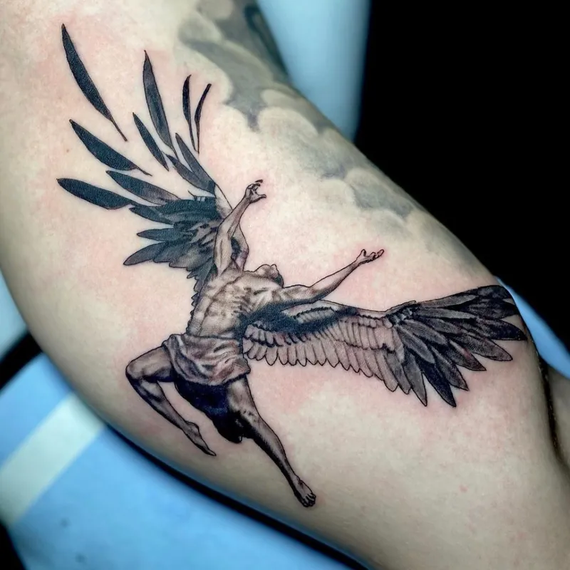 Black and grey tattoo of a winged figure diving headfirst with wings outstretched and arms reaching upward, on the inner forearm.