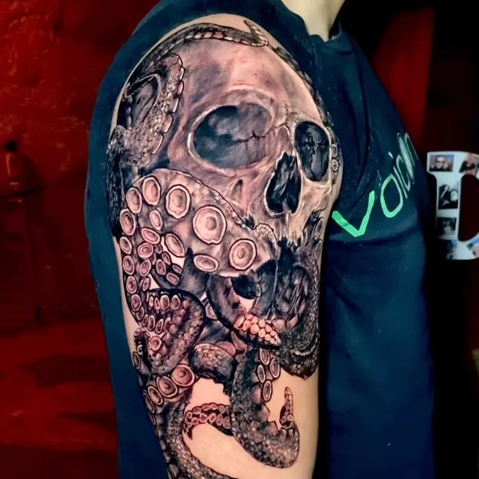 Black and grey realism tattoo of a human skull entwined with octopus tentacles, covering the upper arm and shoulder.