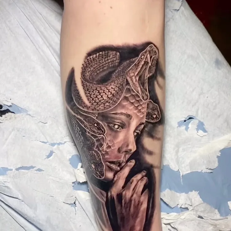 Black and grey realism tattoo of a Medusa-style woman with snakes coiled as hair, resting her chin on her hand, on the forearm.