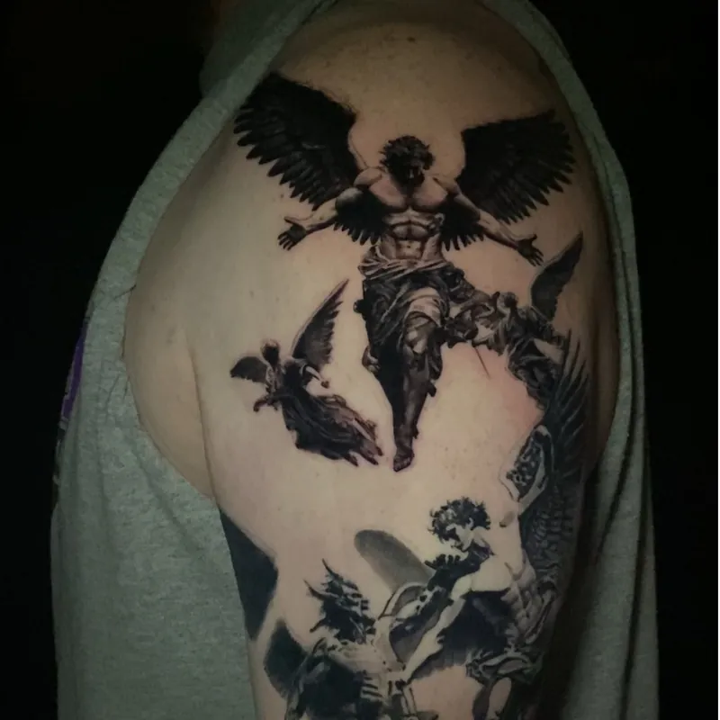 Black and grey tattoo of a large winged figure with arms outstretched above a mythological battle scene with a horned creature, on the shoulder and upper arm.
