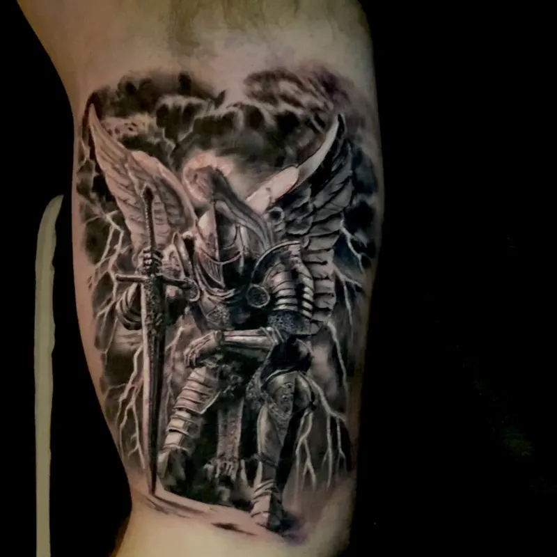 Black and grey realism tattoo of an armored, winged warrior angel wielding a sword amid storm clouds and lightning, on the inner bicep.