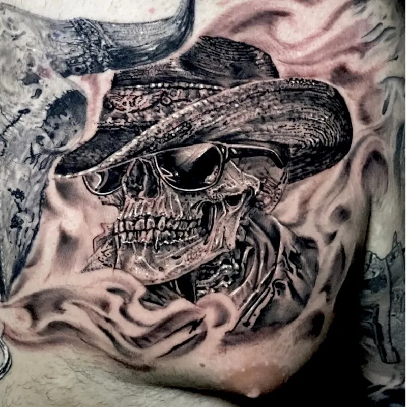 Black and grey realism tattoo of a skull wearing a cowboy hat and sunglasses beneath a curved bull horn, on the chest.