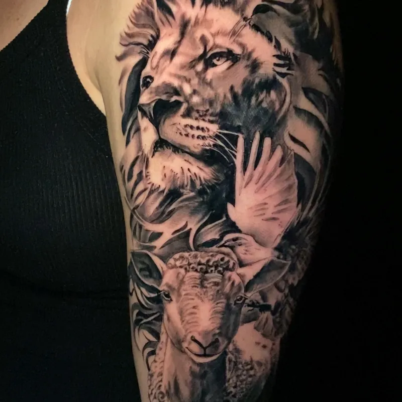 Black and grey realism tattoo of a lion's head merging into a horned ram's head, with a feathered wing motif, on the upper arm.
