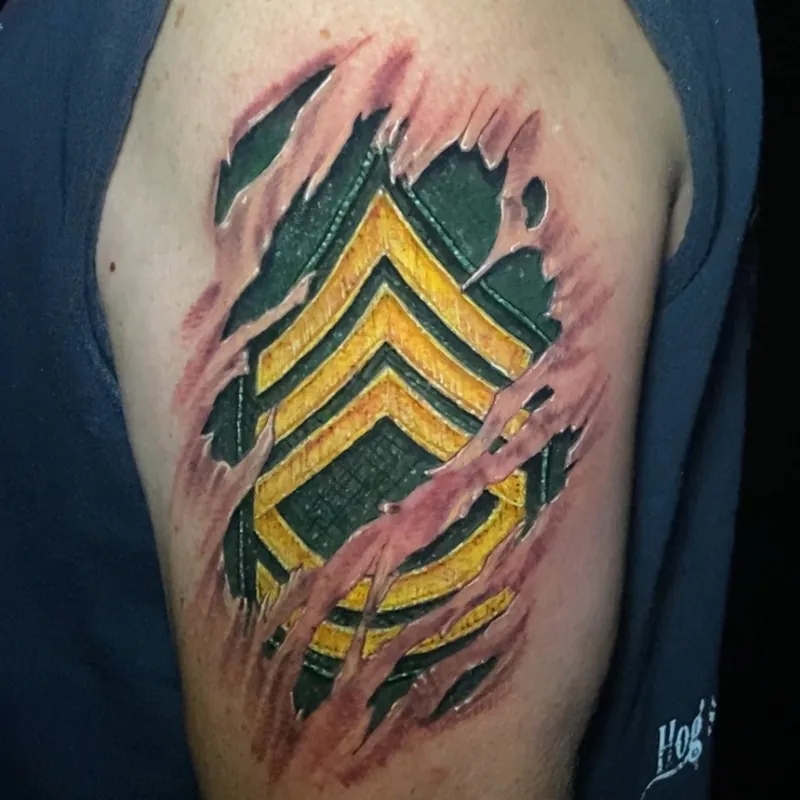 Color tattoo on the upper arm styled as torn skin, revealing a military rank insignia patch with gold chevron stripes on dark green fabric underneath.