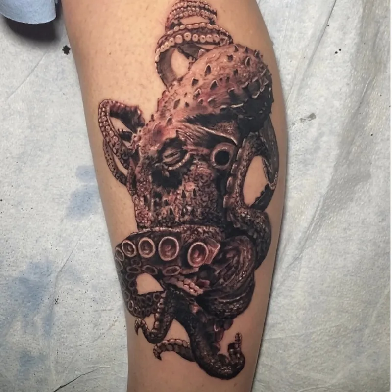 Black and grey tattoo on the calf of a detailed octopus head with textured, bumpy skin and coiled tentacles wrapping around the leg.