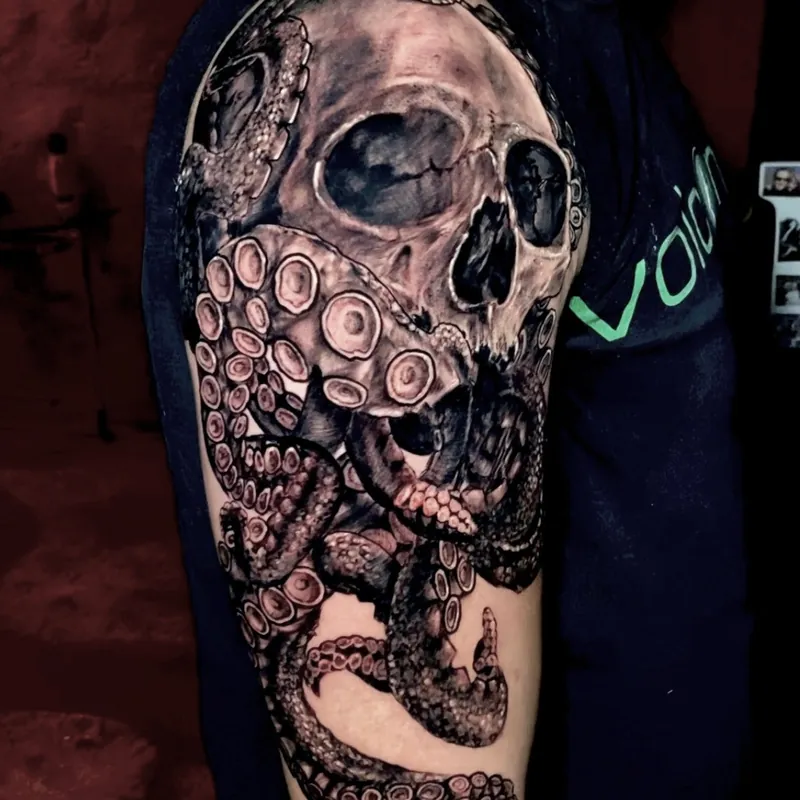 Black and gray realism tattoo of a human skull entwined with octopus tentacles, suckers wrapped through the eye sockets and one tentacle curling below the elbow.