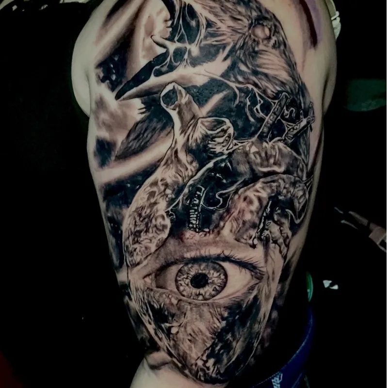 Black and gray tattoo on the upper arm featuring a screeching raven, twisted branches, and a large detailed eye in a dark surreal composition.