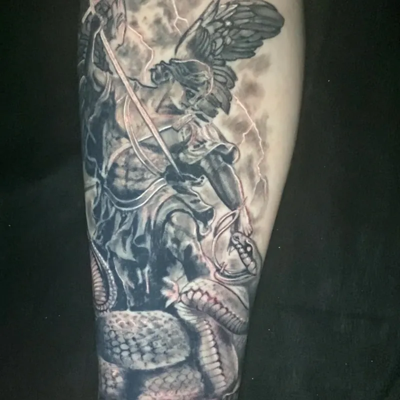 Black and grey realism tattoo of a winged archangel in armor driving a spear into a coiled serpent on broken stone, with lightning behind him, on the forearm.