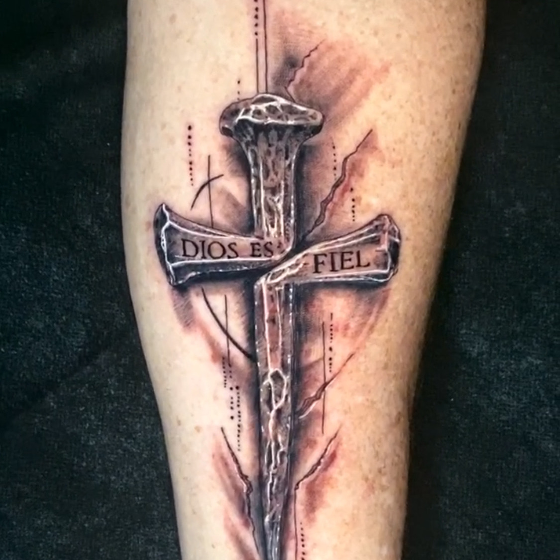 Black and grey realism tattoo of a cross made from a driven iron nail, its crossbeam lettered Dios Es Fiel, with cracks and scratch marks radiating around it, on the forearm.