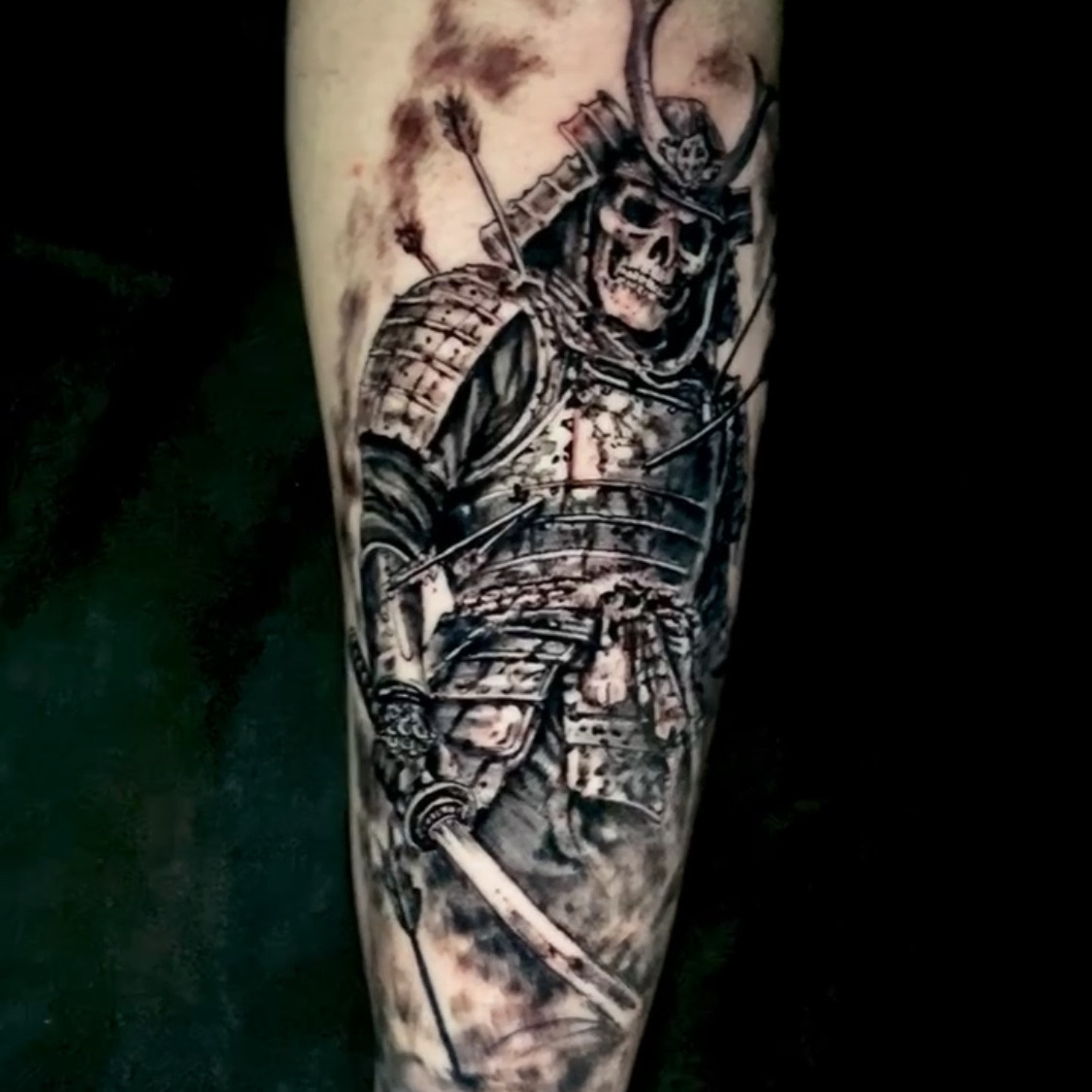 Black and grey realism tattoo of a skeletal samurai in full armor and a horned helmet, arrows lodged in his armor and a katana at his side, on the forearm.