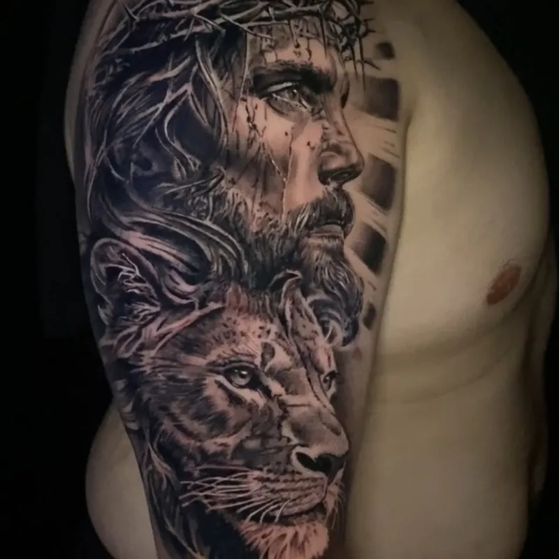 Black and grey realism tattoo of Jesus in a crown of thorns looking upward, with blood running down his face and a lion's head below him, on the upper arm.