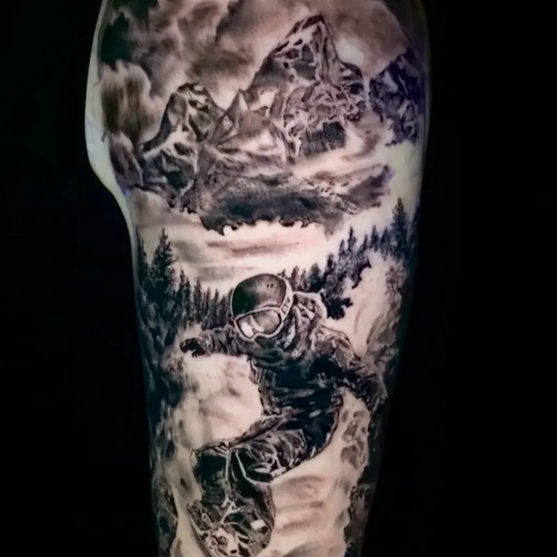 Black and grey realism tattoo of a snowboarder in a helmet and goggles carving through deep snow, with pine trees and a cloud-covered mountain peak above, on the upper arm.