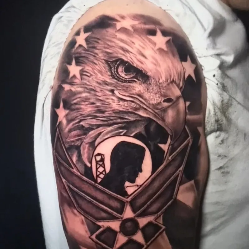 Black and grey realism tattoo of a bald eagle's head ringed with stars above the Air Force winged emblem, with a POW/MIA silhouette at its center and engraved dog tags below, on the upper arm.